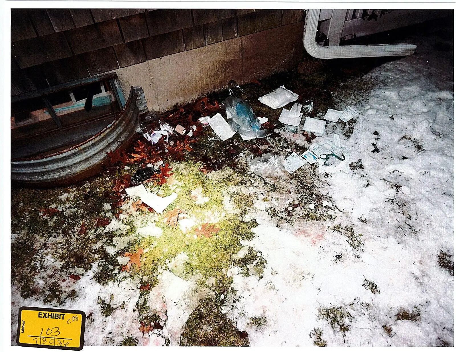 Exhibit 103, an uncropped post-treatment photograph of irregular bare and snowy ground beside the right window well with medical debris and visible staining
