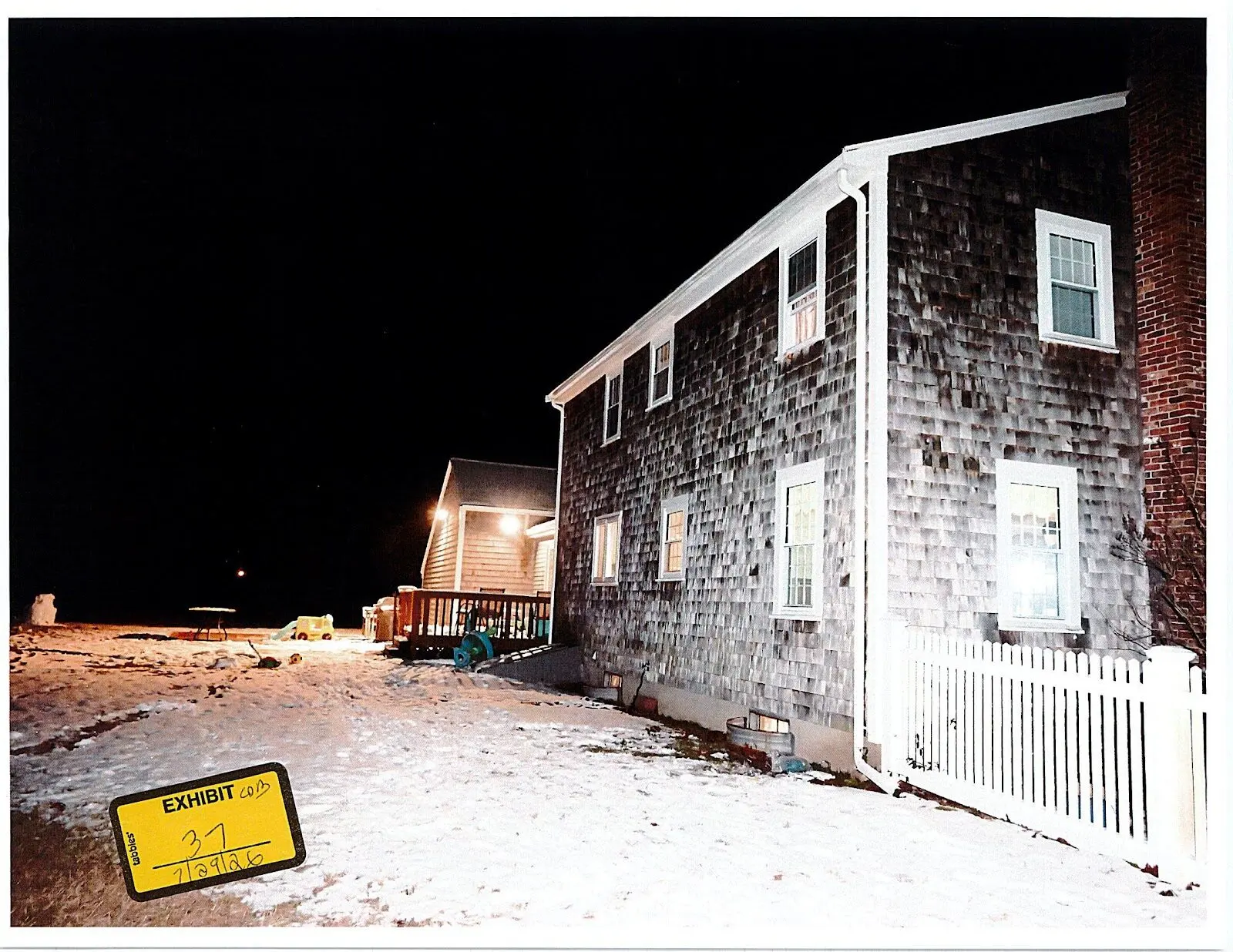 Exhibit 37, an uncropped oblique night photograph showing snow across the rear yard, the deck and turquoise wound hose reel, and the side of the house