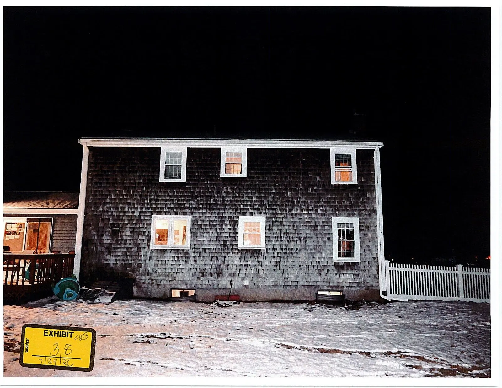 Exhibit 38, an uncropped front-on night photograph of the rear elevation: a turquoise wound hose reel stands beside the deck at far left and a window well is at far right